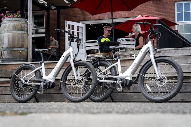 A Pair of White Electric Bikes Parked Near Couple Sitting Outside a Restaurant