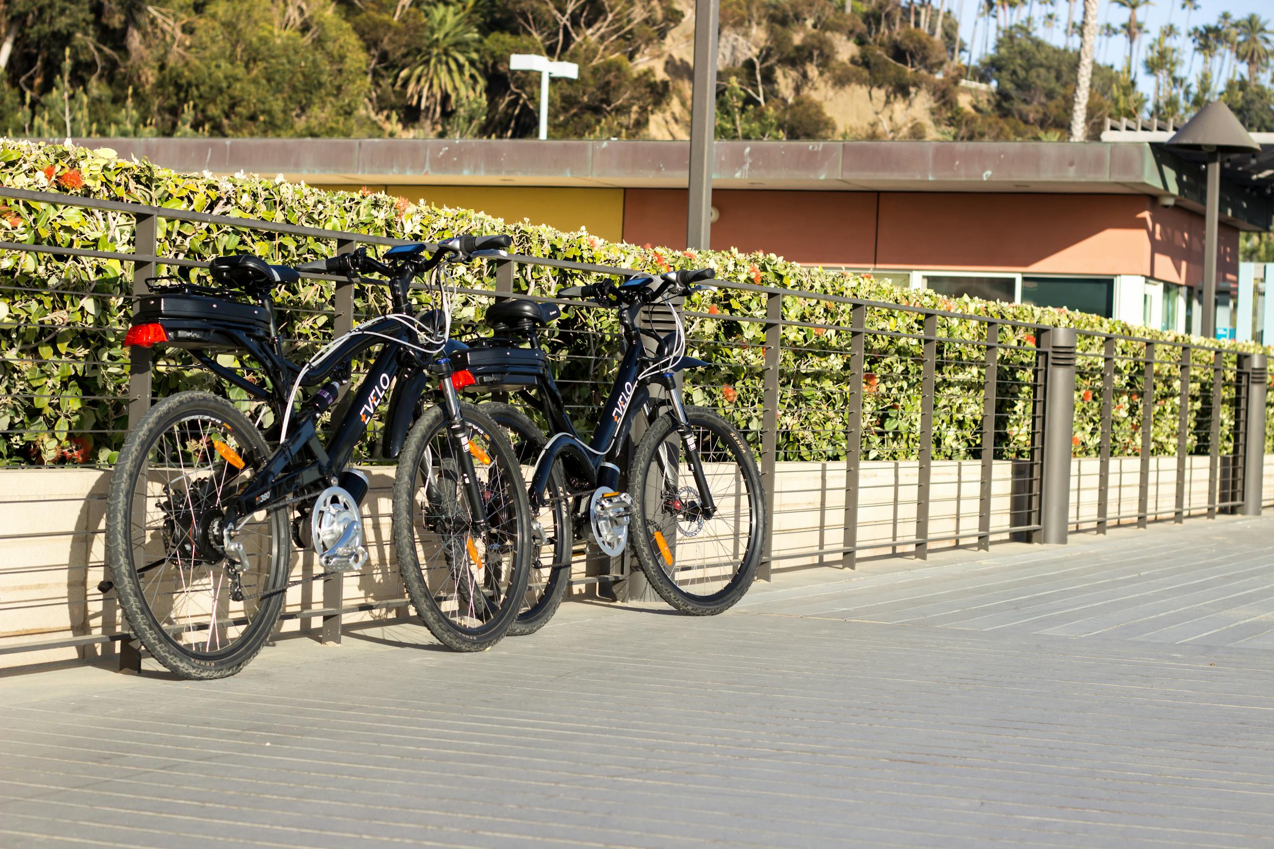 Two electric bikes parked on a railing next to a fence