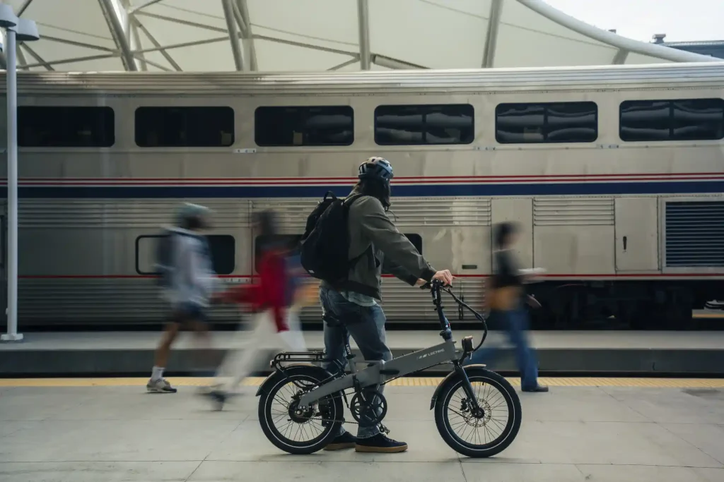 Commuter walking a gray Lectric XP Lite 3 folding electric bike on a train station platform
Copy